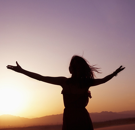 સૂર્યાસ્ત આકાશ સામે વિસ્તરેલા હાથ સાથે સ્ત્રીનું સિલુએટ.